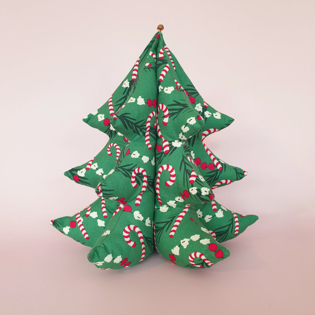 A handmade fabric Christmas tree sits on a pink background. The festive fabric features popcorn and candy canes strung on the tree.