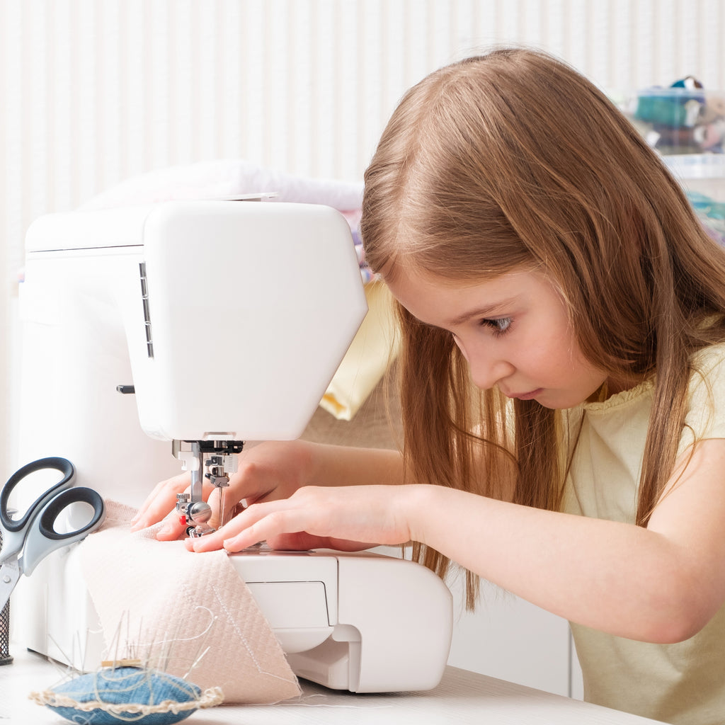 a young girl sews at a sewing machine with a look of concentration on her face