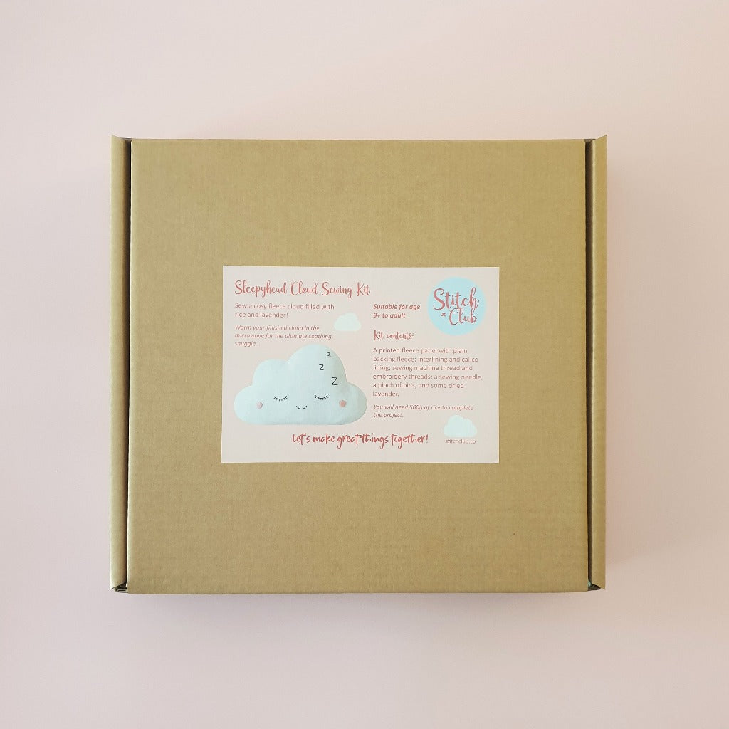 A cardboard box containing supplies for a sewing kit, to make a fleecy kawaii cloud with an embroidered sleepy face.