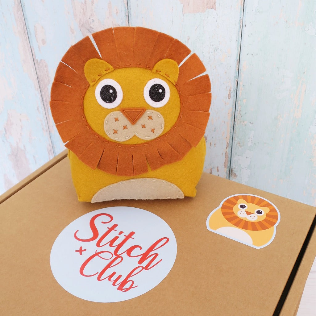 a handmade felt lion toy sits on a sewing kit box