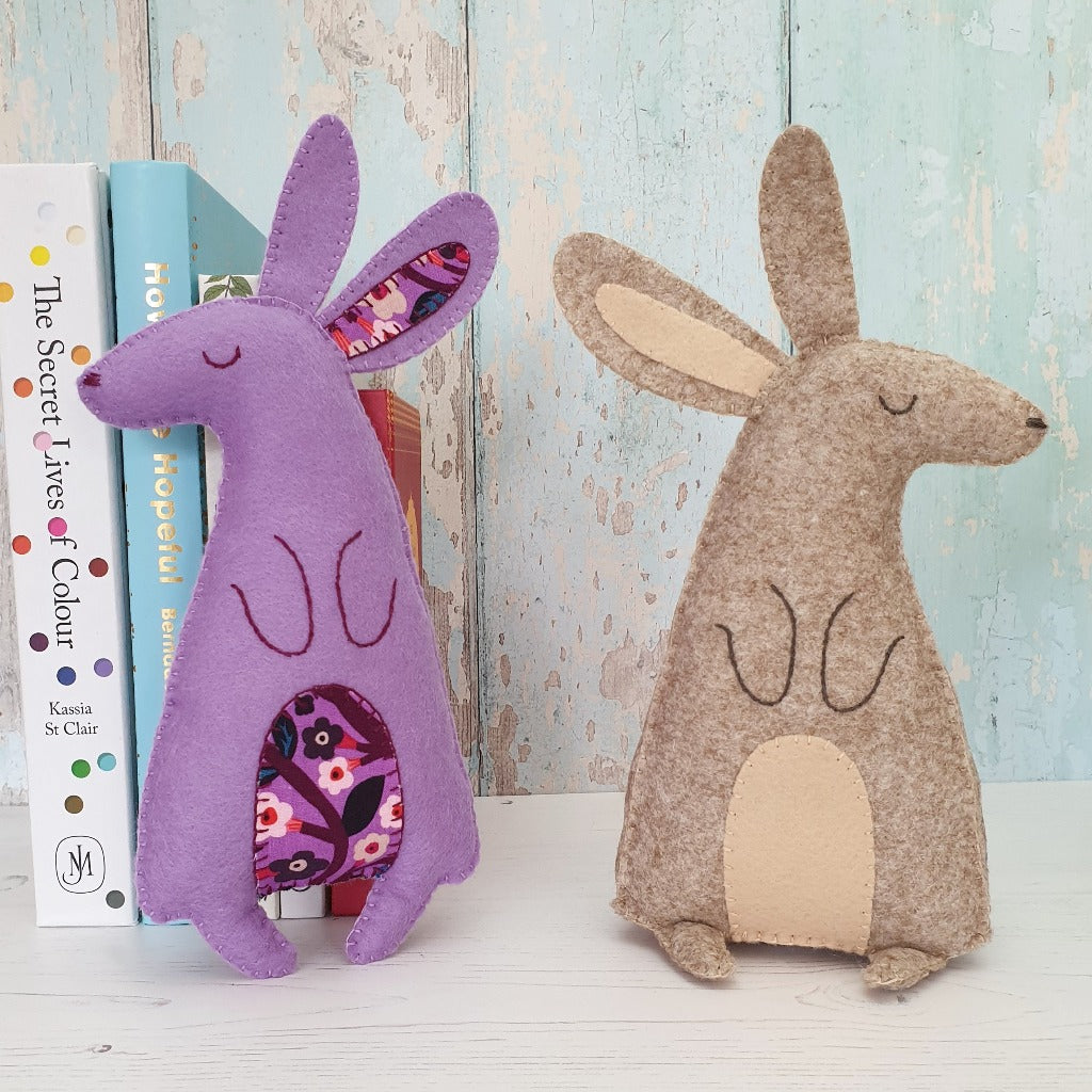 two felt hares sewn by hand, sitting on a shelf with some books