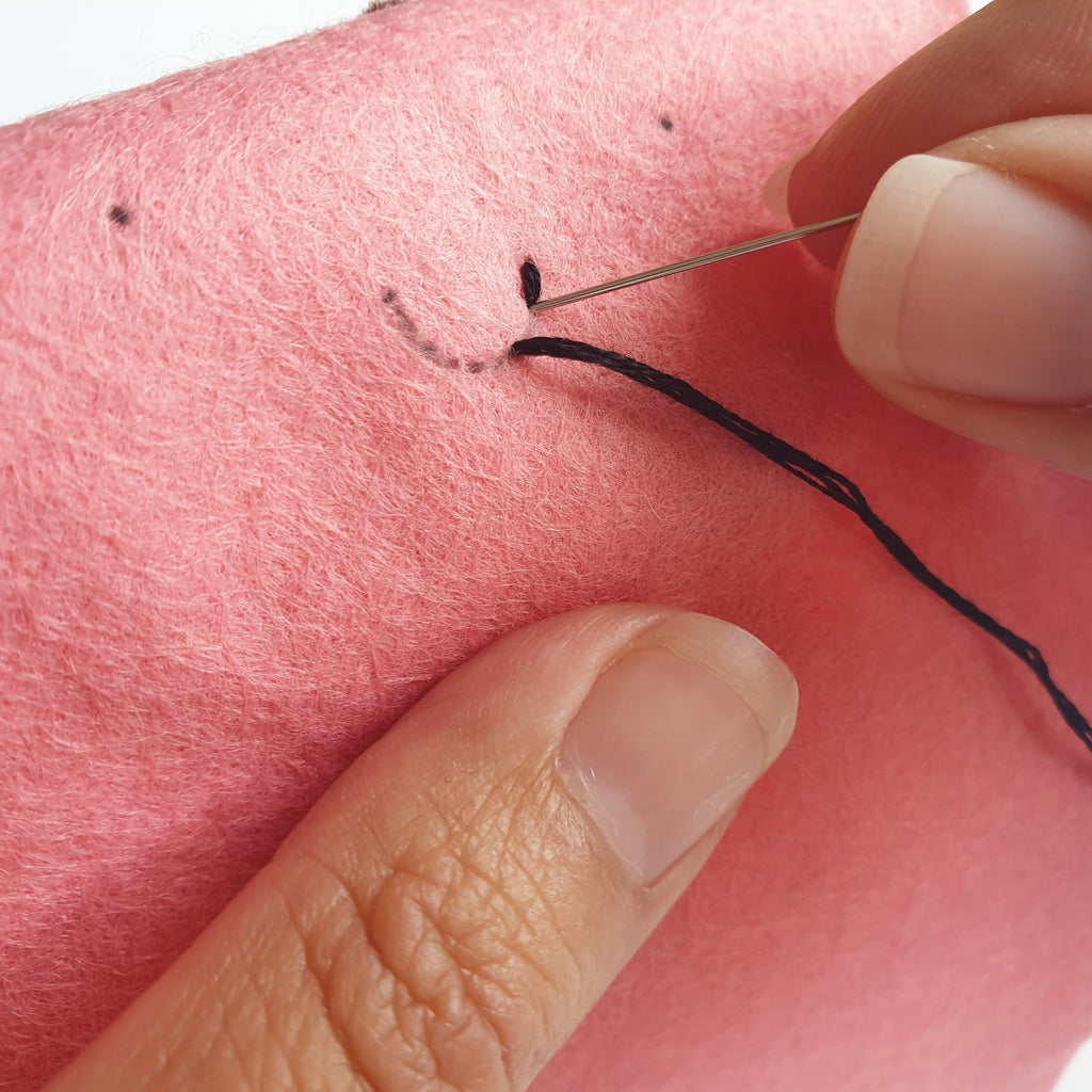 A sewing process photo teaching how to sew backstitch to represent the mouth on a kawaii felt marshmallow.