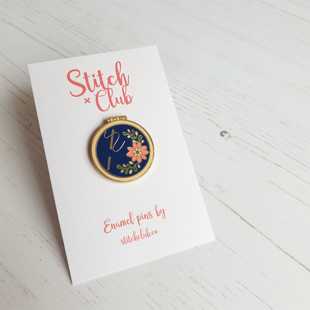 A hard enamel pin badge attached to a card backing from Stitch Club, featuring an embroidery hoop design.