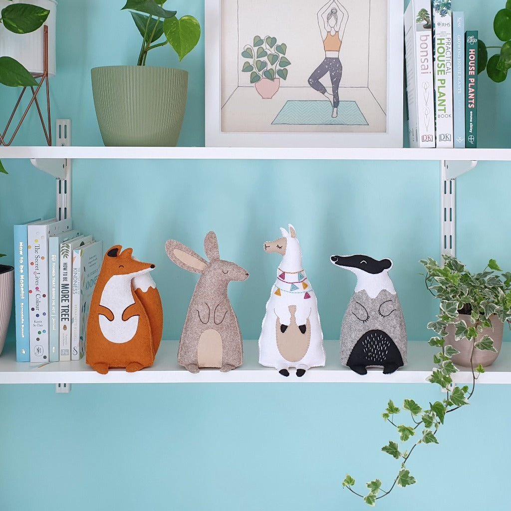 A turquoise wall with white mounted shelves, filled with plants, books, and handmade felt animals