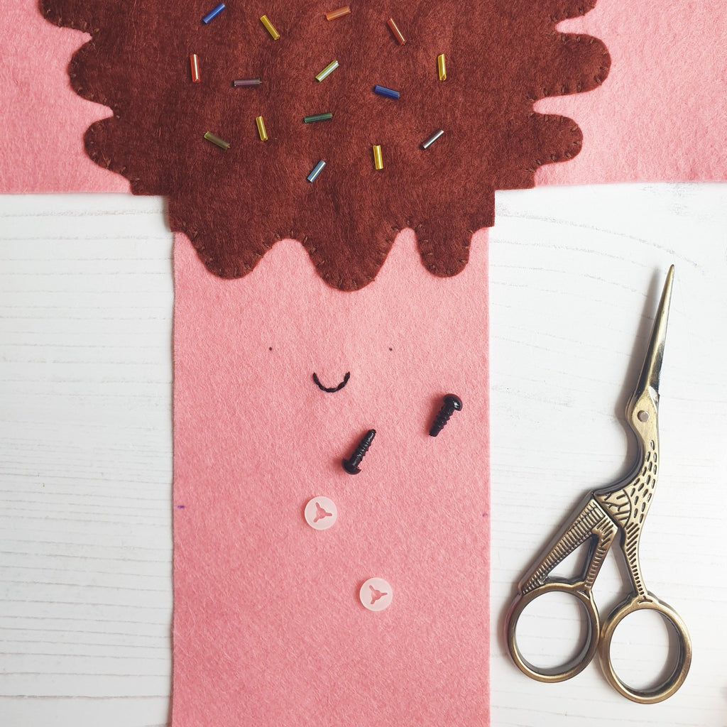 A sewing process photo showing pink and brown felt representing a marshmallow, with sprinkle beads and stork embroidery scissors.