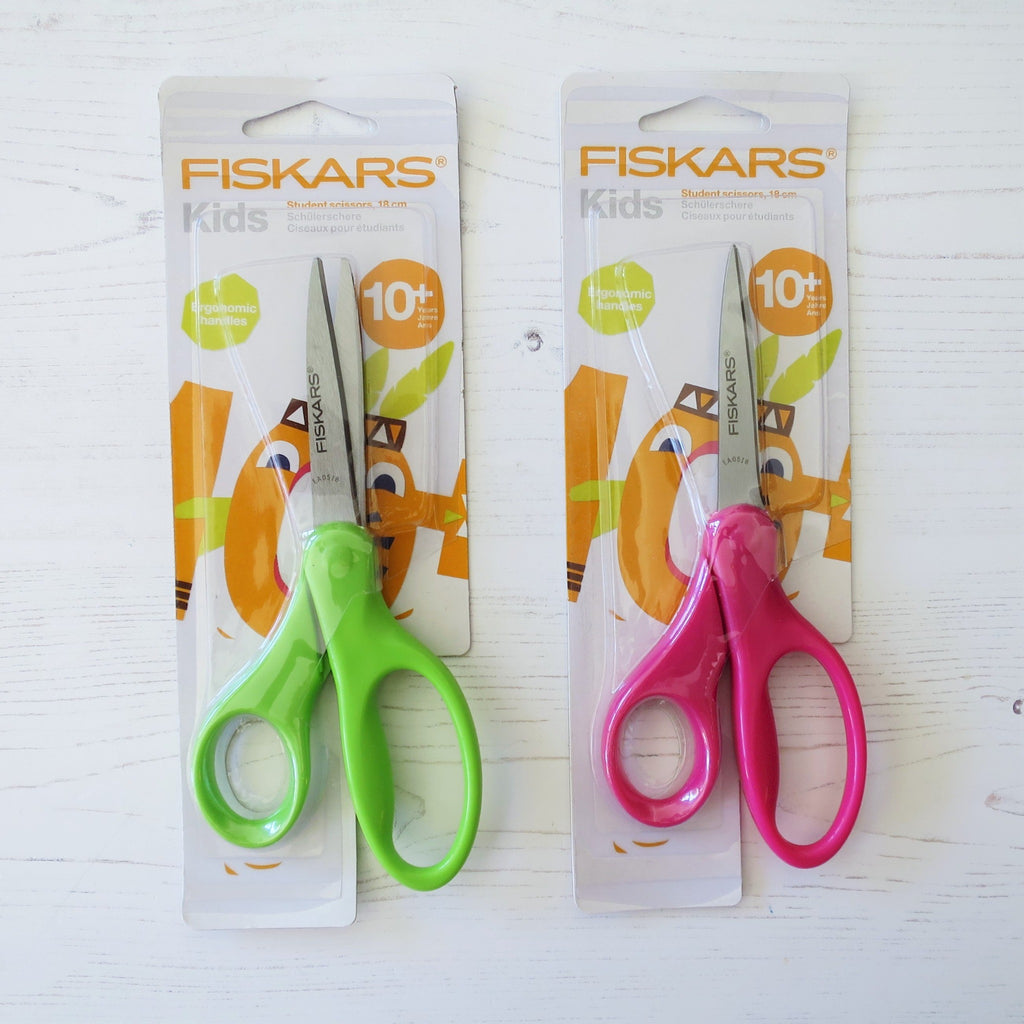 Two pairs of Fiskars student scissors in green and pink, in their packaging.