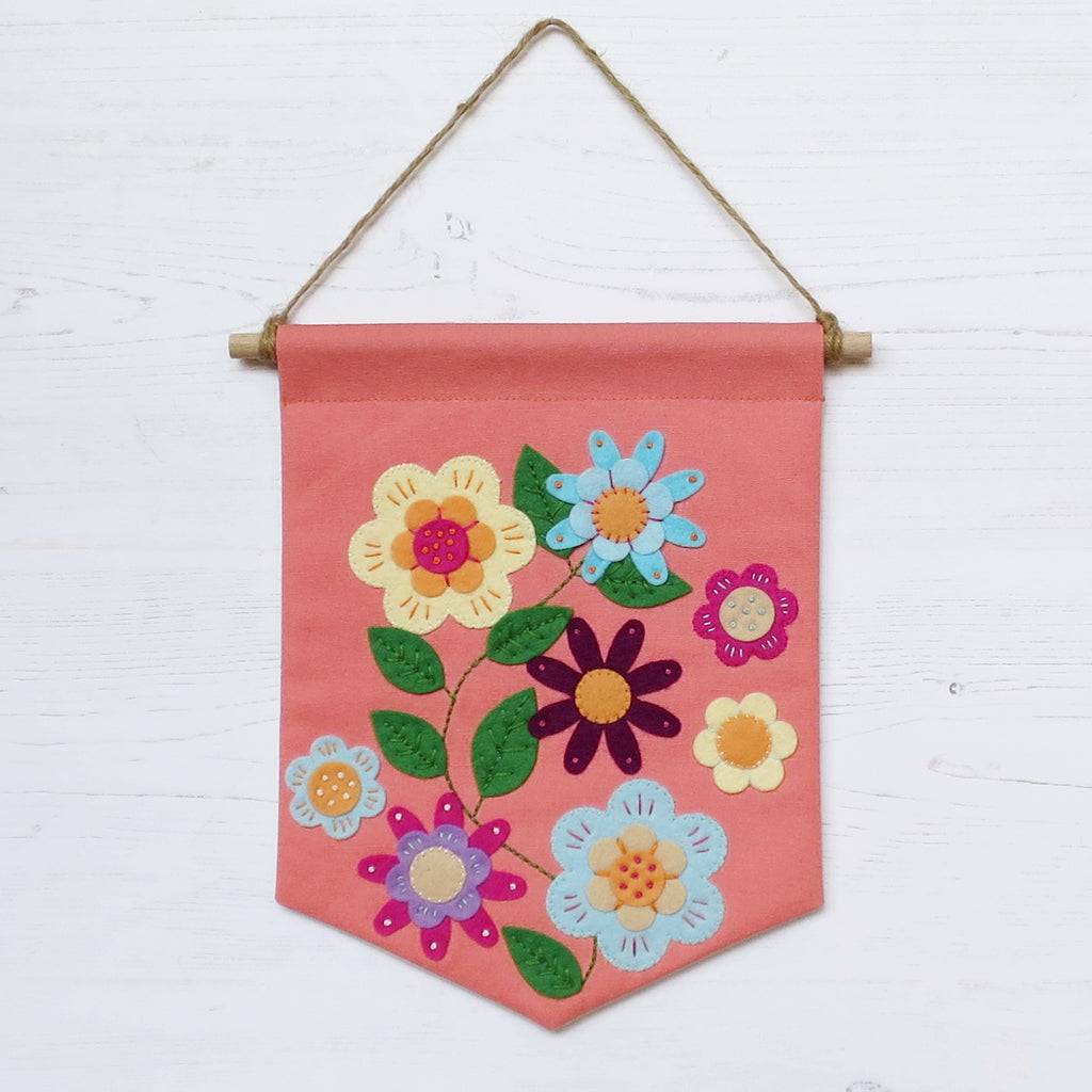 A pinky-orange canvas penant banner hanging from twine. Hand sewn applique felt flowers with embroidery stitches.