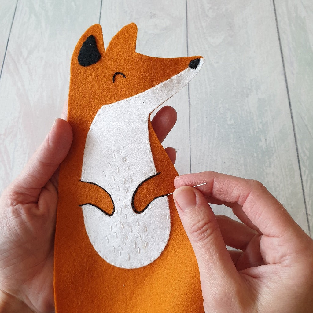 Hands sewing a felt fox character