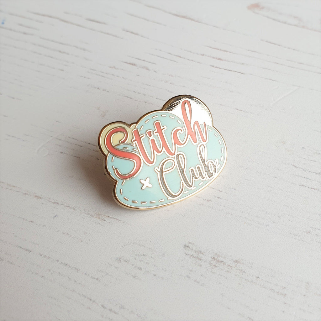 A hard enamel pin badge featuring the logo of Stitch Club sewing kit  designer.