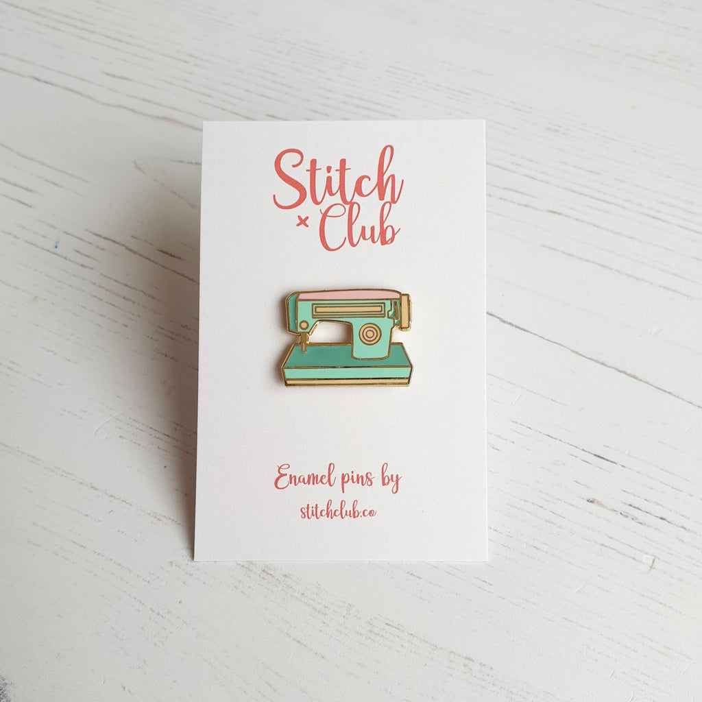 A hard enamel sewing machine pin badge, featuring and 1950s style sewing machine in mint greens and pink with gold plating.